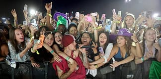 小賈斯汀魅力橫掃Coachella 預告:很快再見 Male singer in a red beanie performs at a crowded concert, fans reach over the barrier with phones raised around him.