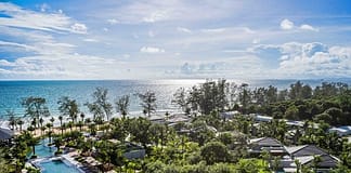 從旅遊到貿易:富國島星灣皇冠假日酒店為2027年APEC峰會搭建舞台 Aerial view of a tropical resort with a long pool, palm trees, and white buildings beside a blue sea on a sunny day.