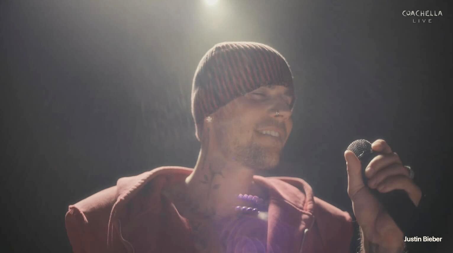 Justin Bieber performs on stage at Coachella, wearing a striped beanie and maroon hoodie, holding a mic under bright lights (Coachella Live).”]} {
